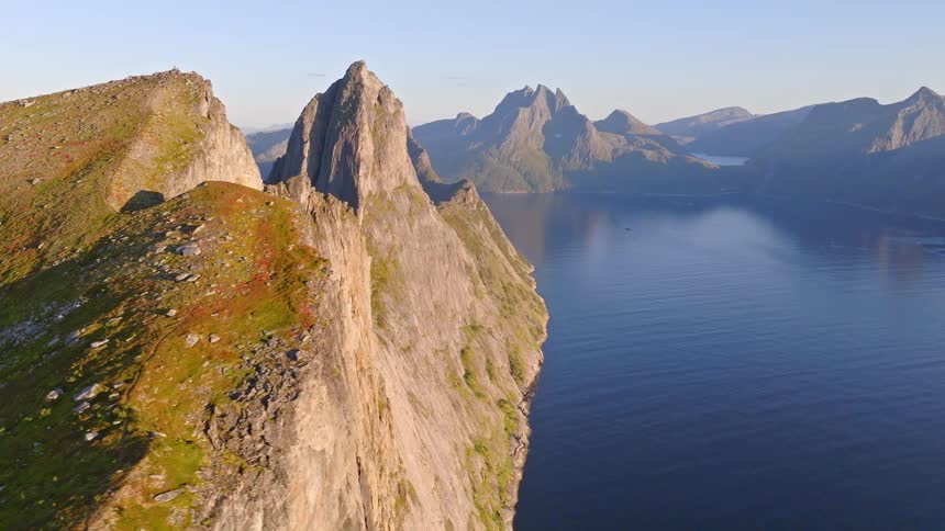 A breathtaking aerial shot pans along a rugged mountain ridge, revealing the sheer cliffs and deep blue waters of a majestic fjord at sunrise