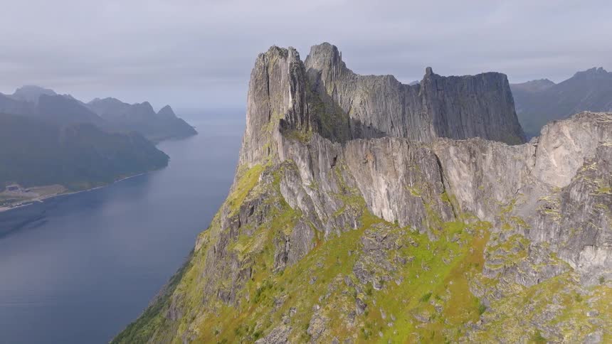 A stunning aerial ascent reveals the majestic and rugged Segla mountain on the island of Senja, Norway, towering over the vast fjord below