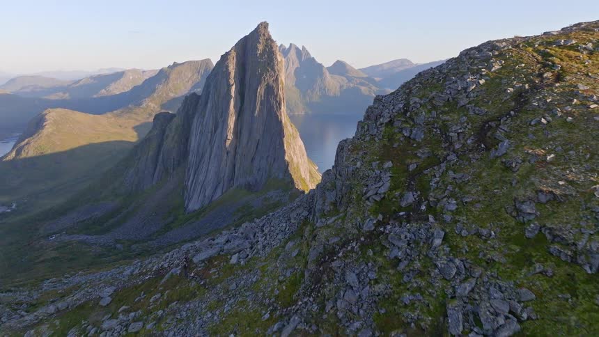Aerial view flying along a rocky mountain ridge towards the iconic Segla peak overlooking a fjord in Senja, Norway