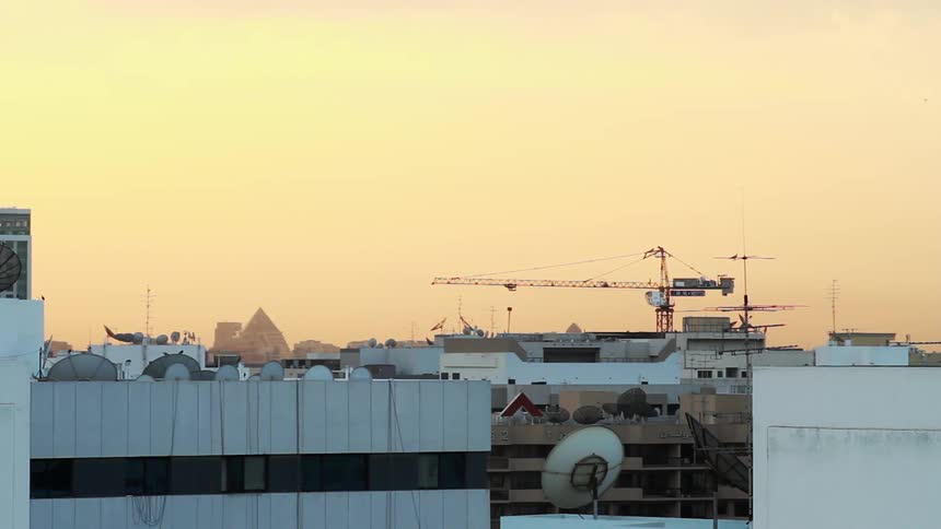A large crane rotates in a city at sunset