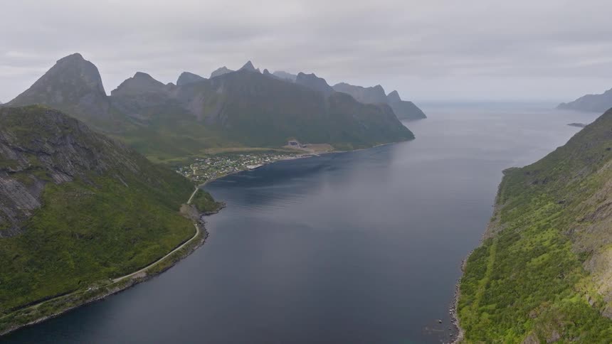 Epic aerial pullback reveals a vast Norwegian fjord surrounded by dramatic, rugged mountains and a secluded coastal village