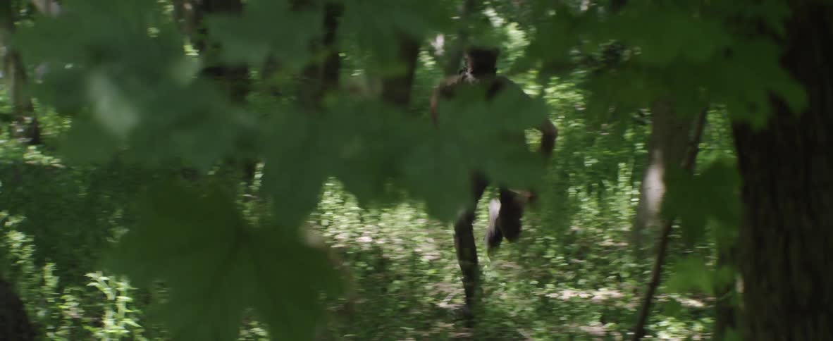 A man with camouflage paint on his face runs after another person in the forest
