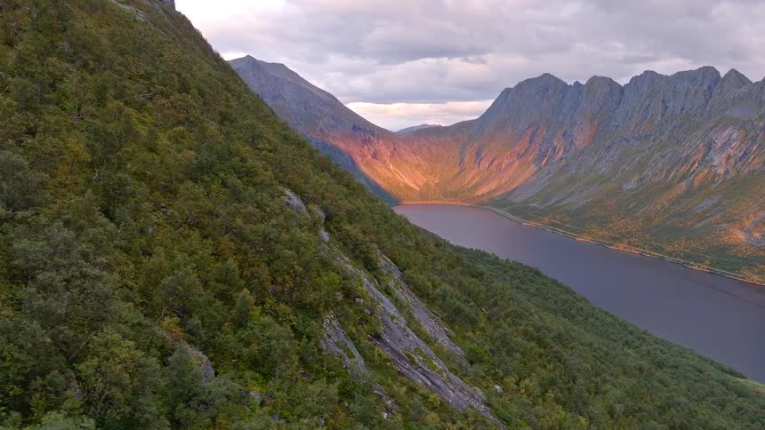 Epic aerial reveal of a majestic fjord in Norway, with mountains bathed in the warm glow of a beautiful sunset