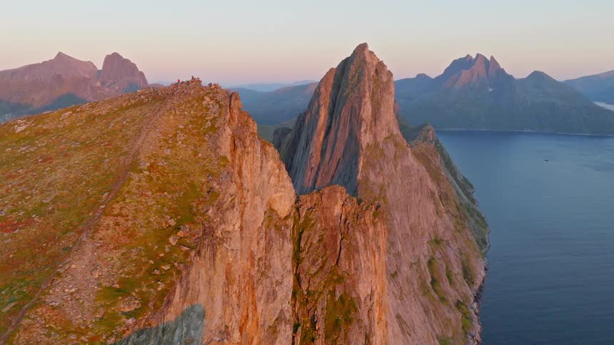 A stunning aerial view reveals a dramatic mountain ridge and steep cliffs dropping into the ocean during a golden sunset