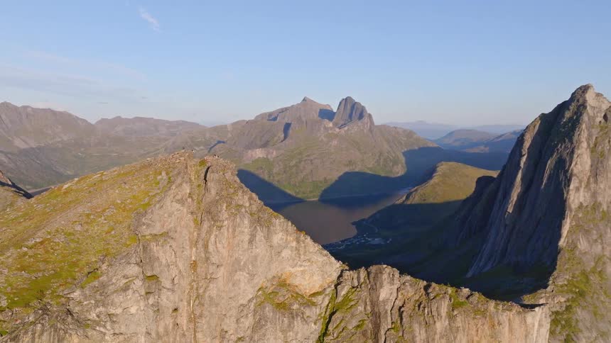 A stunning aerial view pulls back from a mountain ridge to reveal the dramatic and iconic Segla peak in Senja, Norway