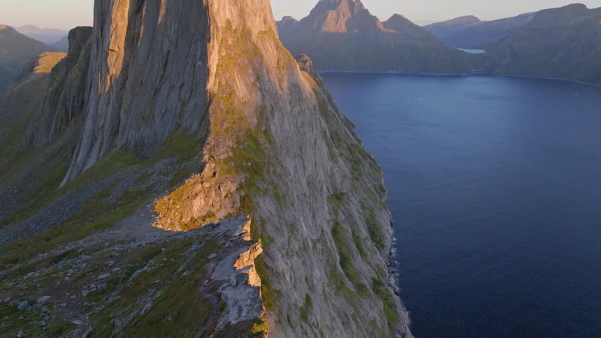 A stunning aerial view tilts up to reveal the iconic Segla mountain on the island of Senja, Norway, its golden cliffs dropping dramatically into the fjord at sunset
