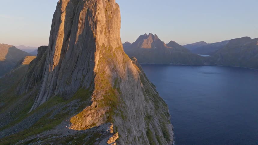 An epic aerial tilt-up reveals the majestic Segla mountain on Senja island in Norway, bathed in golden hour light with a fjord below