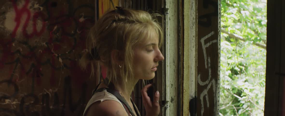 A woman looks out a window of a broken down house