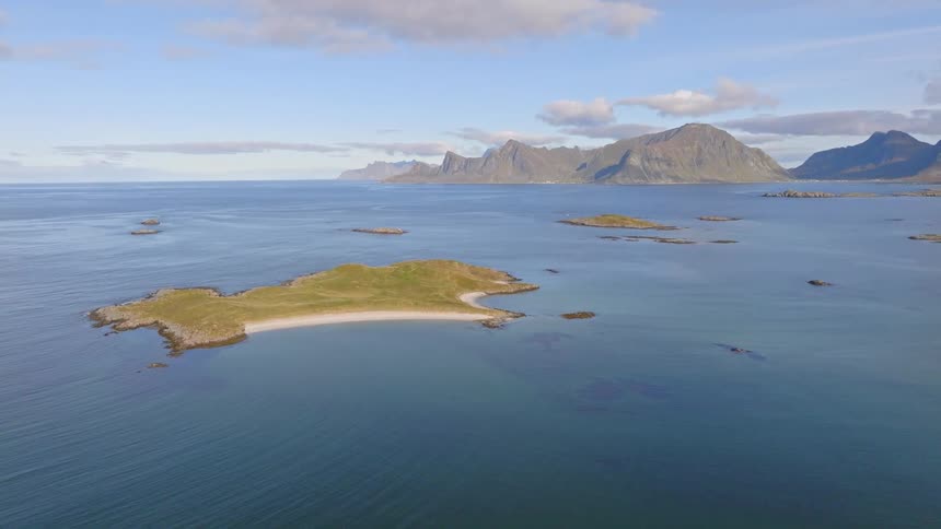 A stunning aerial view captures a small, secluded island with a sandy beach in the calm sea, with a dramatic mountain range on the horizon
