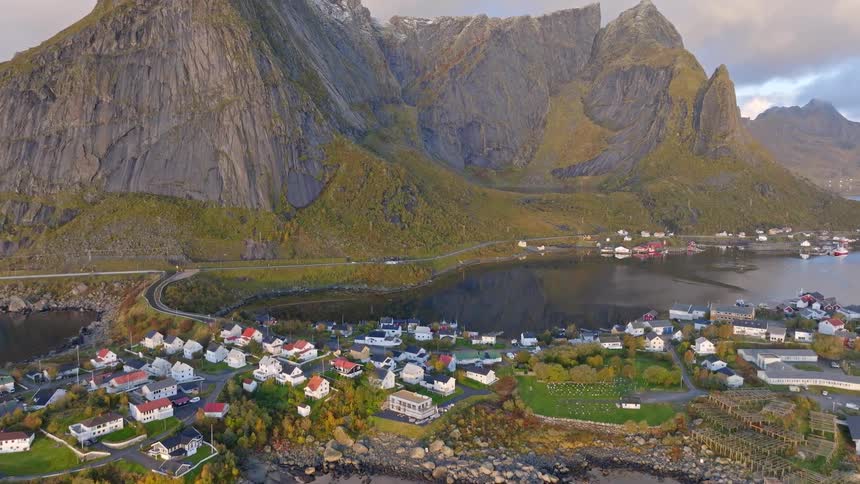 An aerial view reveals the stunning landscape of a small fishing village nestled at the foot of massive mountains in the Lofoten Islands, Norway