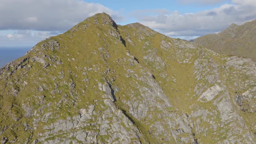 Epic aerial flight over a green and rocky mountain ridge reveals a stunning coastal landscape with a remote village below