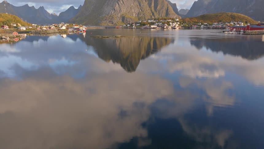 An aerial tilt reveals the stunning Norwegian fishing village of Reine and its perfect reflection in the calm waters of the fjord