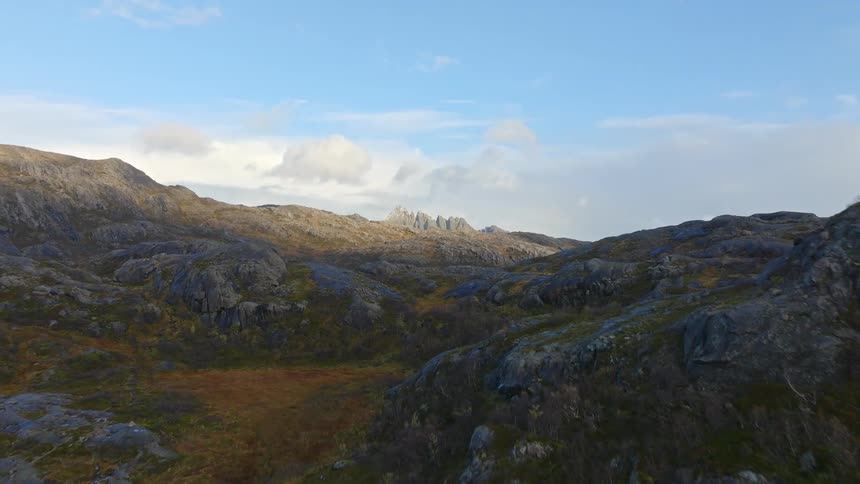 An epic aerial flight ascends over a rugged, mossy landscape to reveal a stunning sunlit mountain range
