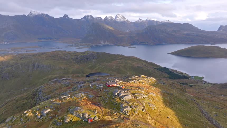 An epic aerial reveals remote cabins on a vast Norwegian fjord overlooking a snow-capped mountain range