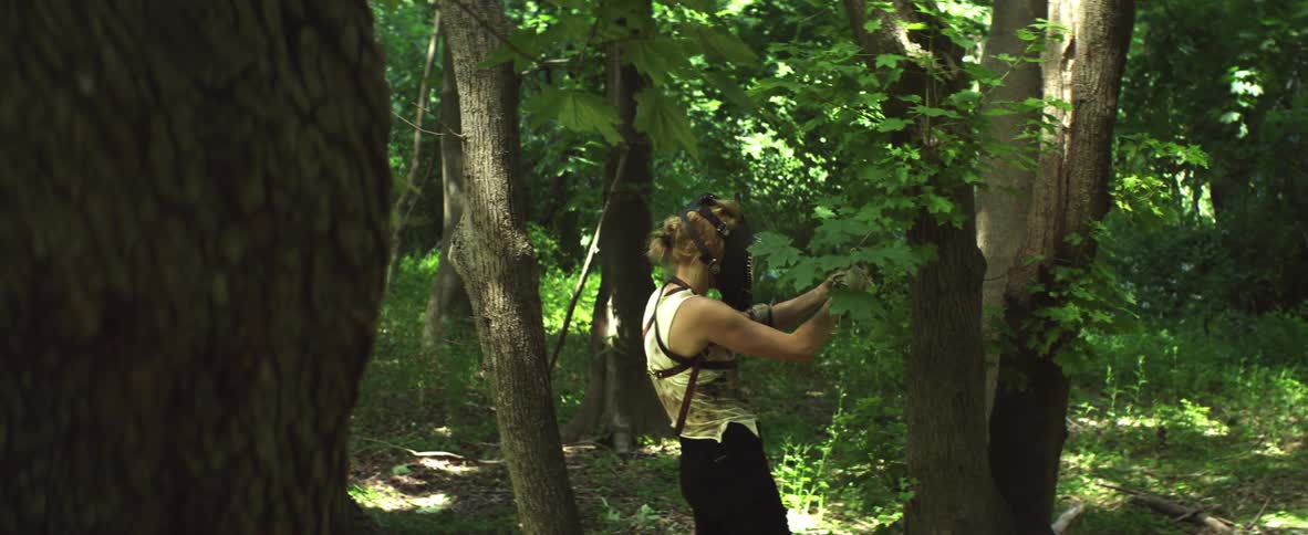 A woman wearing a mask in the forest stops to fasten something to a tree branch