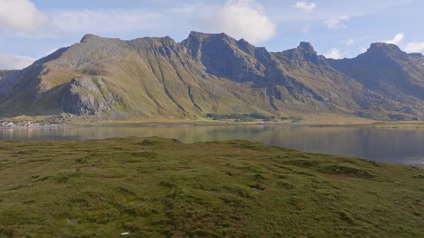 Slow aerial pullback over a calm lake reveals a stunning reflection of the majestic mountain landscape in Norway