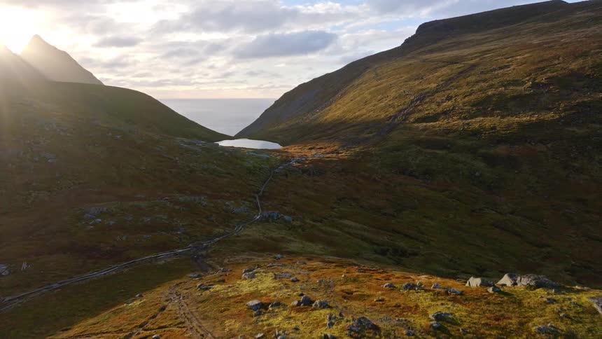 A stunning aerial view flying through a majestic mountain valley towards a serene lake and the ocean during a golden sunset