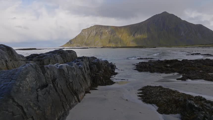 Slowly advancing over the rocky and sandy shore of a Norwegian fjord as the tide gently rises towards the majestic mountains