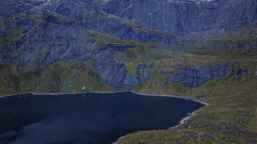 Epic aerial view of a car driving along a scenic mountain road next to a lake with snow-capped peaks in the Lofoten Islands, Norway