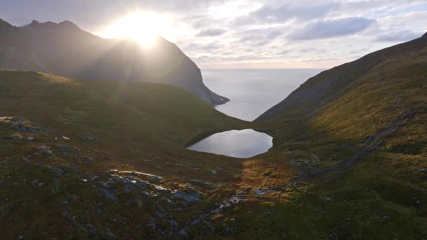An aerial view captures a stunning sunset over a mountain valley, revealing a tranquil lake that leads to the vast ocean