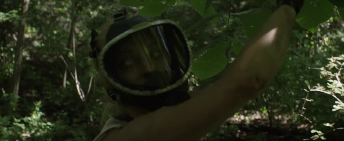 A woman in a mask ties a string to a tree branch in the woods