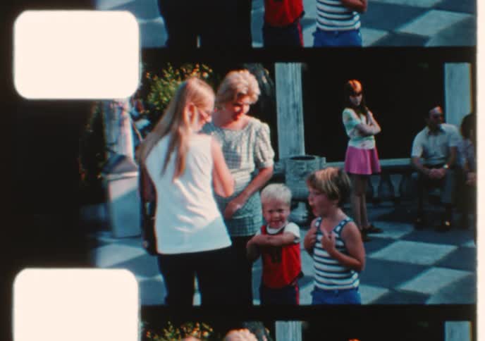 Archival footage from the 1970s shows a family with young children enjoying a day out at a park with an ornate stone fountain