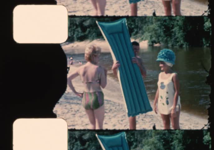 Vintage 1960s home movie shows a family enjoying a summer day swimming and sunbathing at a sandy river beach