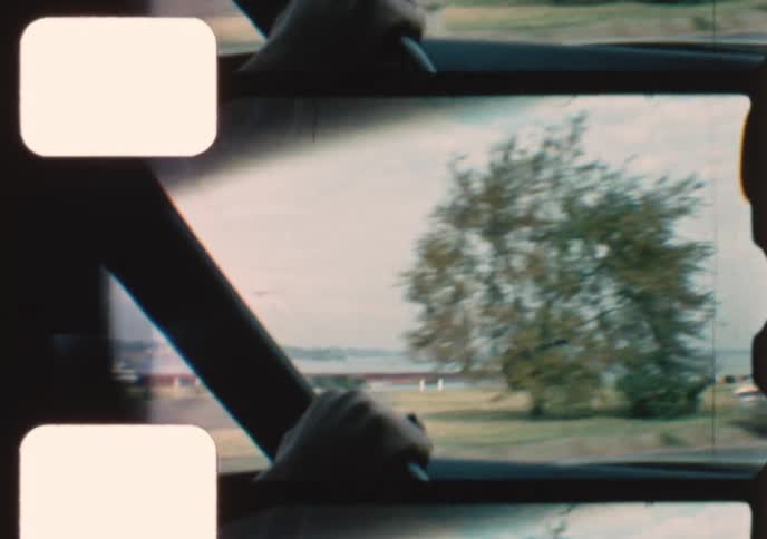 Vintage 8mm film captures the view from a moving car driving along a scenic coastal highway with boats on the water