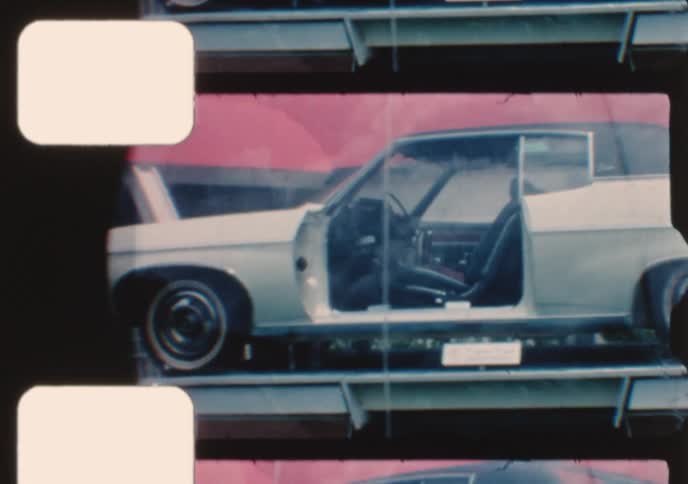 Vintage film captures classic 1970s American cars, including a custom model in a bubble, rotating on display at an outdoor auto show