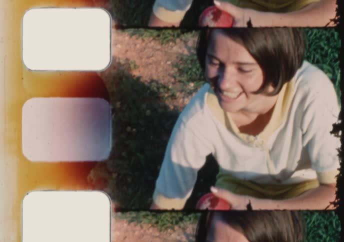 A smiling young woman picks an apple and pets her dog in a park in this charming vintage 8mm home movie
