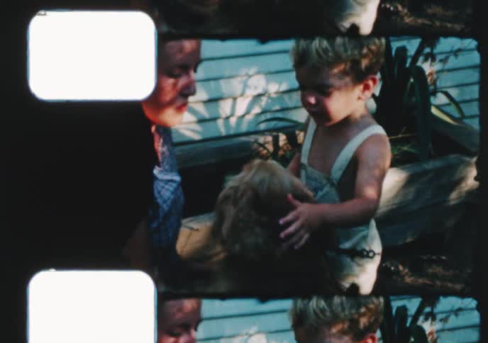 Vintage footage shows a little boy in overalls and a woman petting their beloved cocker spaniel dog in a sunny backyard