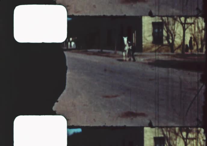 Vintage 8mm film captures a young boy riding a white horse down a dusty street in a quiet old town