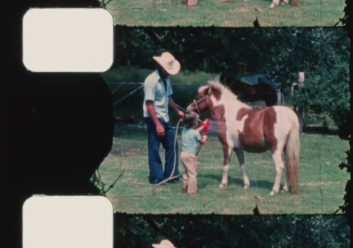Archival footage shows a father in a cowboy hat and his son washing their small pony with a water hose