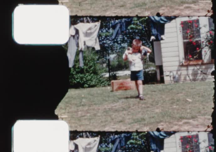 Vintage 8mm home movie footage shows a smiling young boy holding two adorable puppies in his backyard