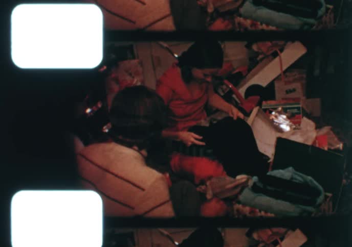 A happy family gathers on the floor to unwrap presents on Christmas day in this charming vintage footage