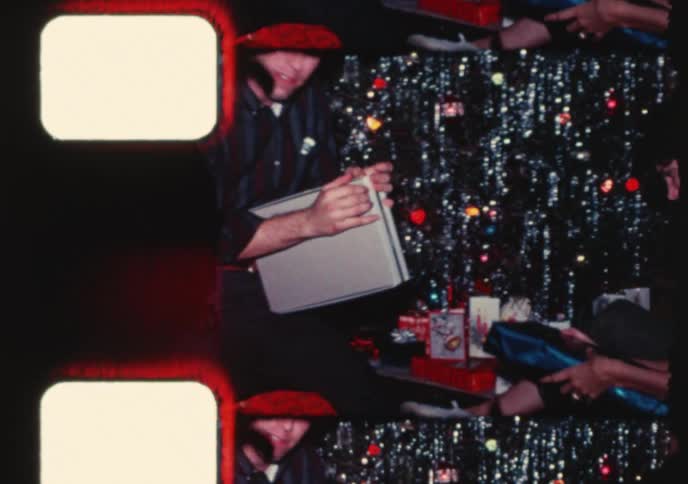 Vintage 8mm home movie captures a family joyfully exchanging and opening presents around a tinsel Christmas tree in the 1960s