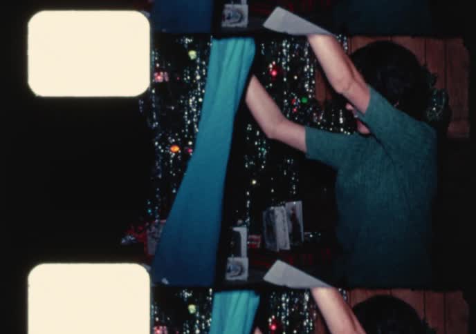Vintage 8mm footage captures a happy man and woman opening their Christmas gifts by a tinsel-covered tree in the 1960s