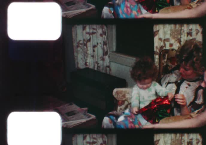 Sweet toddlers excitedly open presents with their family on Christmas morning in this charming 1970s home movie footage