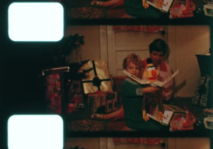 A mother helps her young son unwrap his Christmas presents, including a Bert puppet, in this nostalgic 8mm home movie from the 1970s