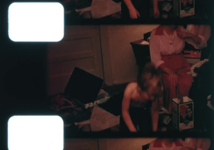 Vintage home movie footage shows a young boy in his pajamas joyfully opening presents with his family on Christmas morning