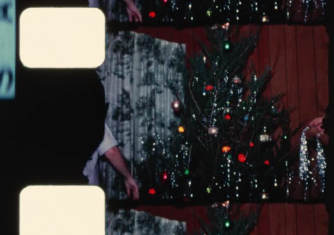 A family gathers to decorate their Christmas tree with colorful ornaments and silver tinsel in this nostalgic 1960s home movie