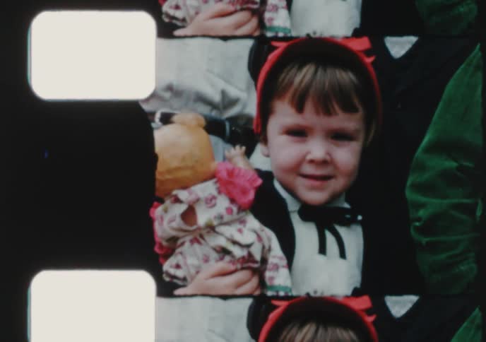 An archival scan of a film strip featuring a cute little girl in a costume smiling and holding a doll