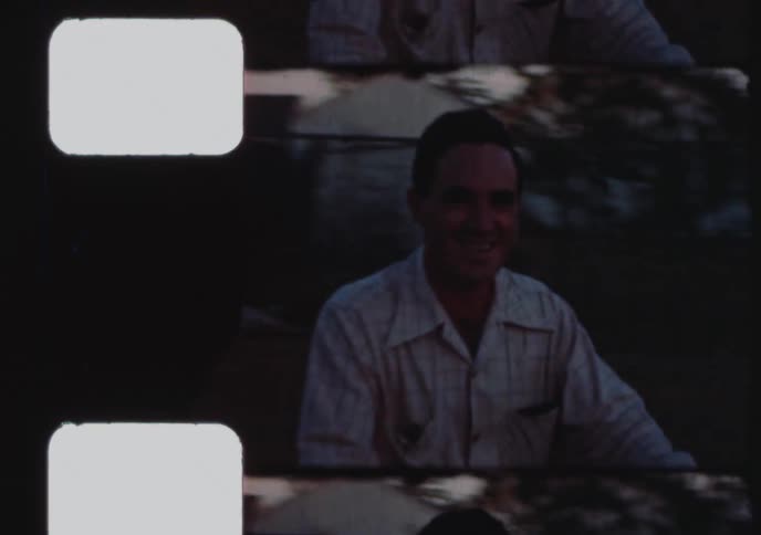 An archival 8mm home movie captures a smiling man sitting on his scooter in a backyard during the evening