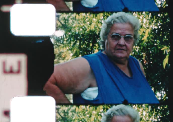 Close-up archival footage captures an elderly woman with glasses and white hair looking at the camera outdoors