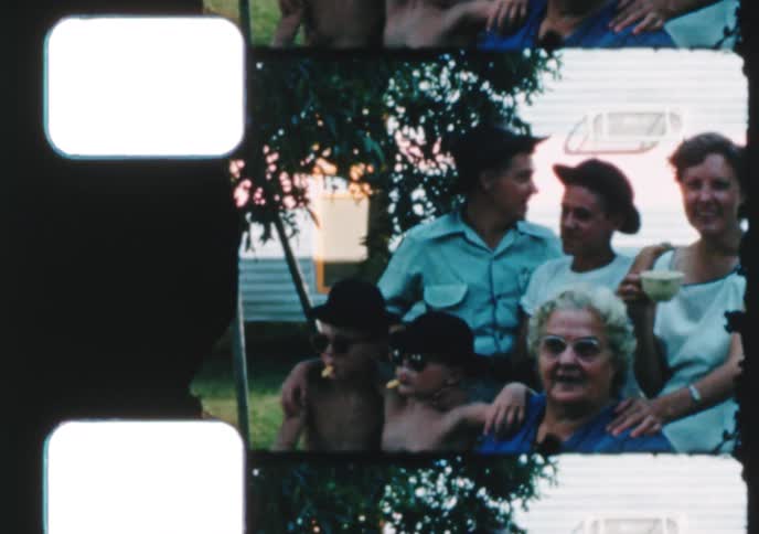 A vintage film strip shows a happy, multi-generational family posing together outdoors by their trailer during a summer gathering