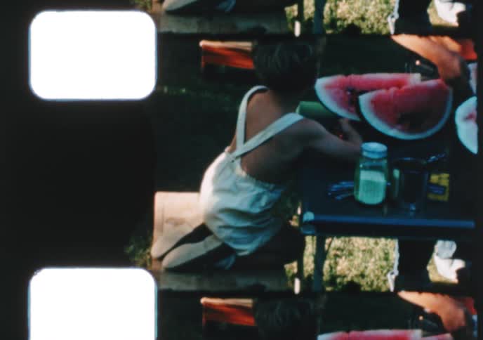 Vintage 8mm film shows a cute little boy in overalls enjoying sliced watermelon at a sunny summer picnic