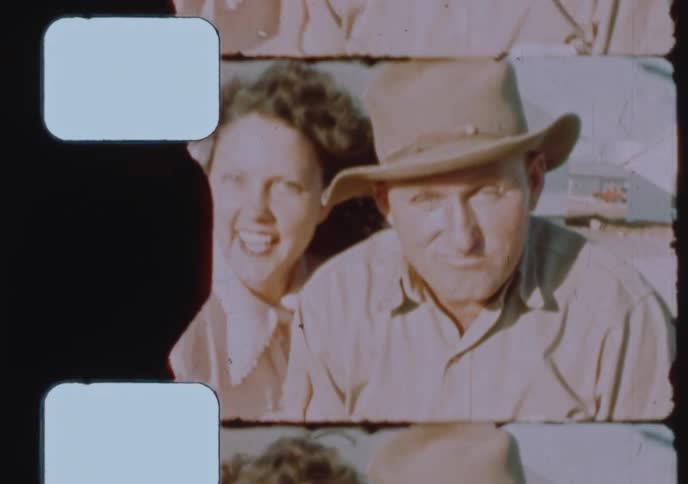 A vintage 16mm film scan captures a happy 1950s couple playfully posing and laughing outdoors