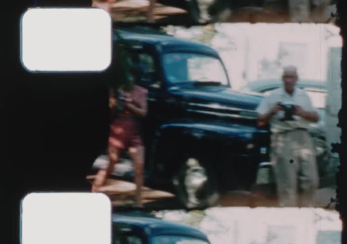 An old film strip captures a man and woman taking photos next to a vintage pickup truck