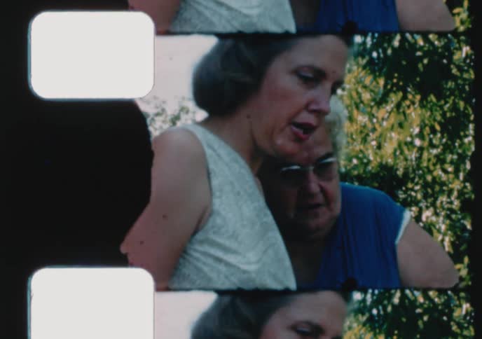 An authentic vintage home movie shows a close-up of two women talking and interacting outside