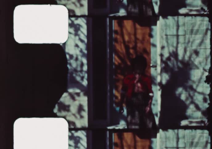 A smiling woman in a red cardigan steps out from a doorway in a nostalgic 8mm home movie from the 1960s